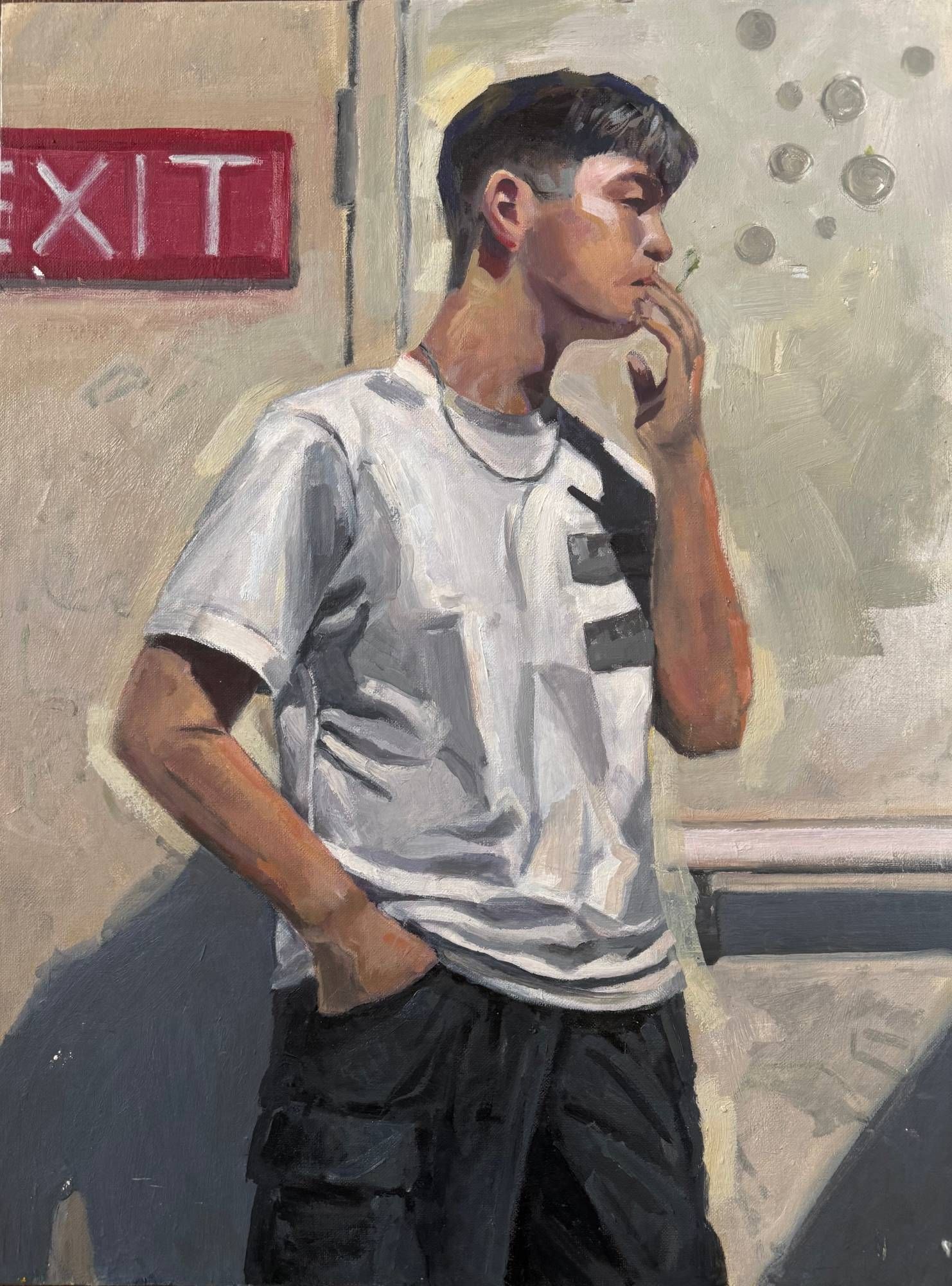 Oil painting of a young man in a white T-shirt and dark cargo pants, one hand in his pocket and the other raised to his mouth, standing in profile against a cream wall with a red EXIT sign at upper left and strong diagonal shadows.