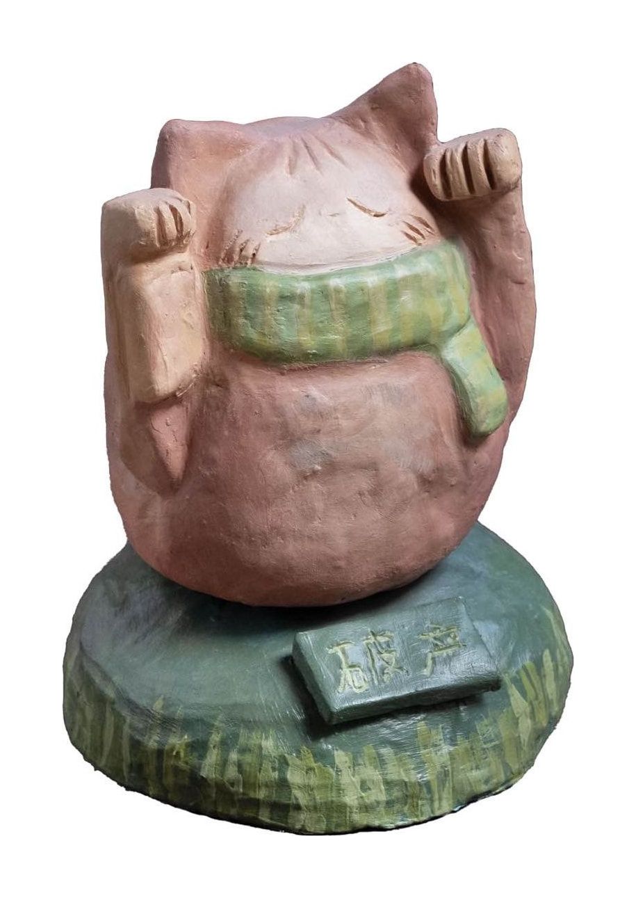 Three-quarter view of the same ceramic cat on its green base, with the sign visible at the front.